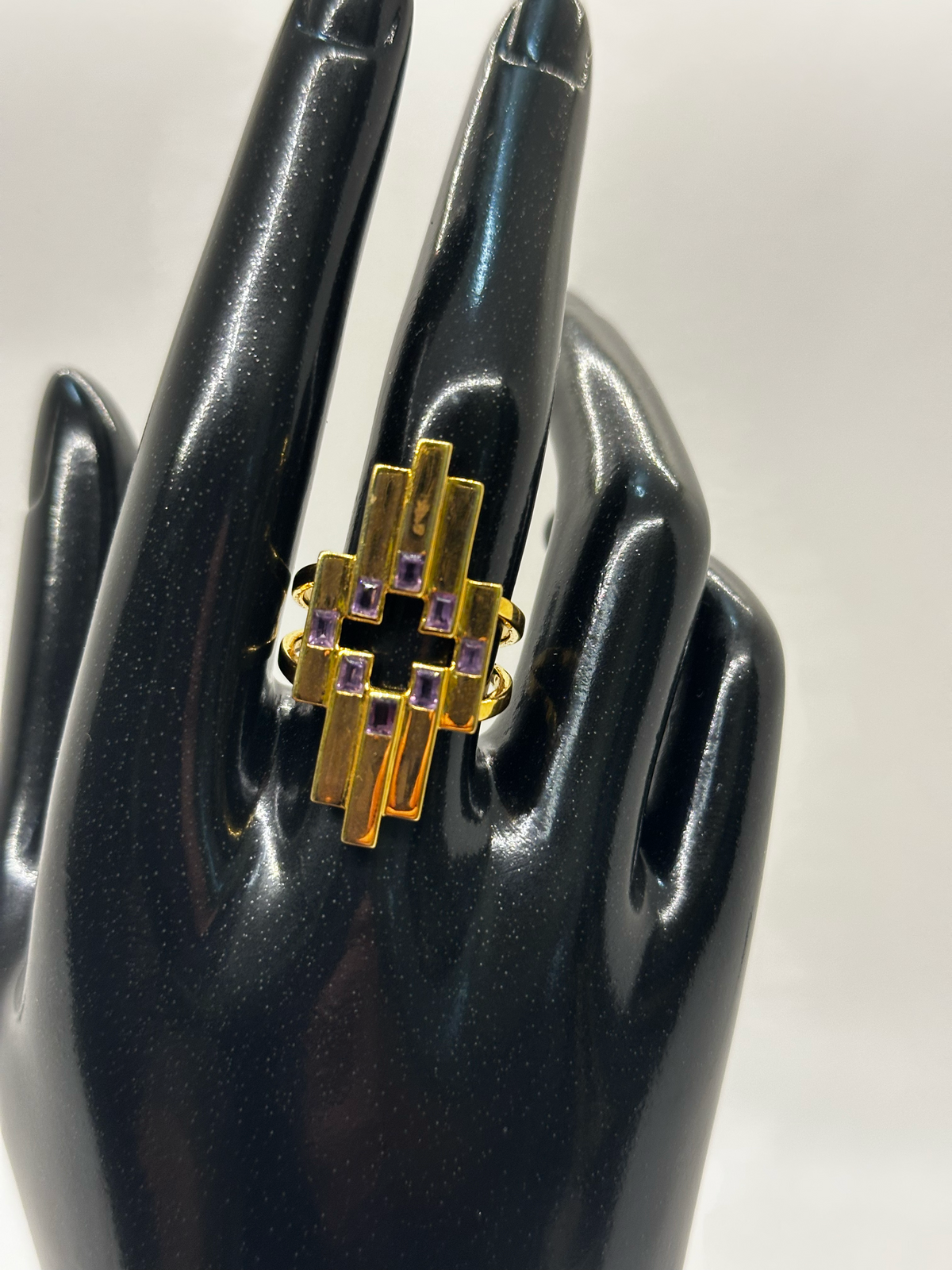 Gold ring with purple gemstones on a black mannequin hand against a white background